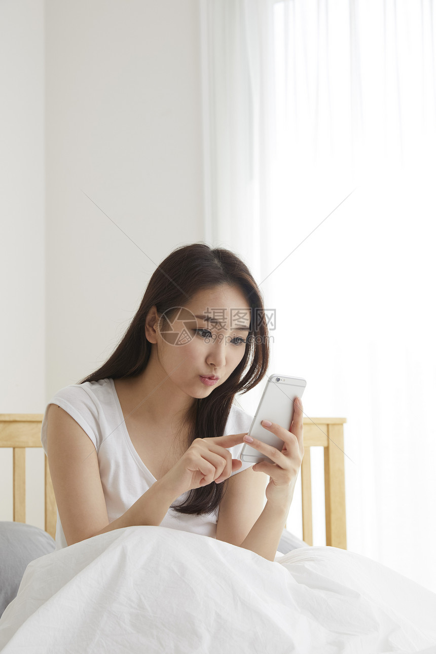 床上玩手机的年轻女性图片