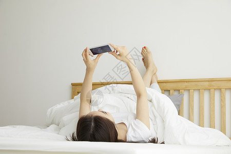 周末躺在床上玩手机的年轻女子图片