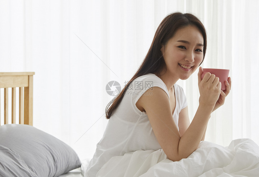 床上拿着水杯微笑的年轻女性图片