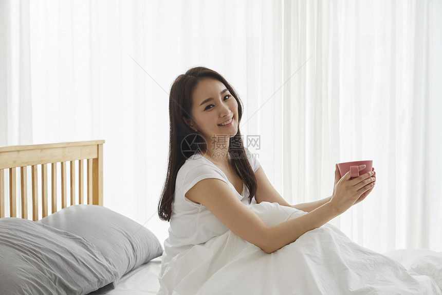 床上捧着水杯的年轻女子图片