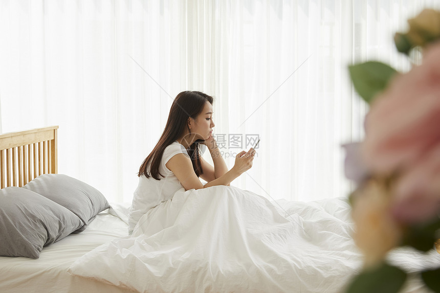 坐在床上玩手机的年轻女性图片