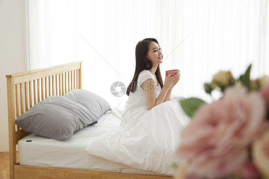 床上捧着咖啡的年轻女性图片