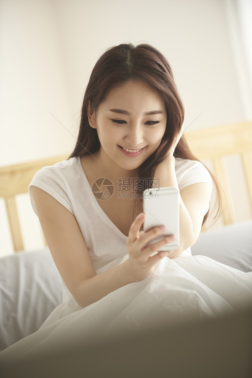 床上使用手机的年轻女子图片