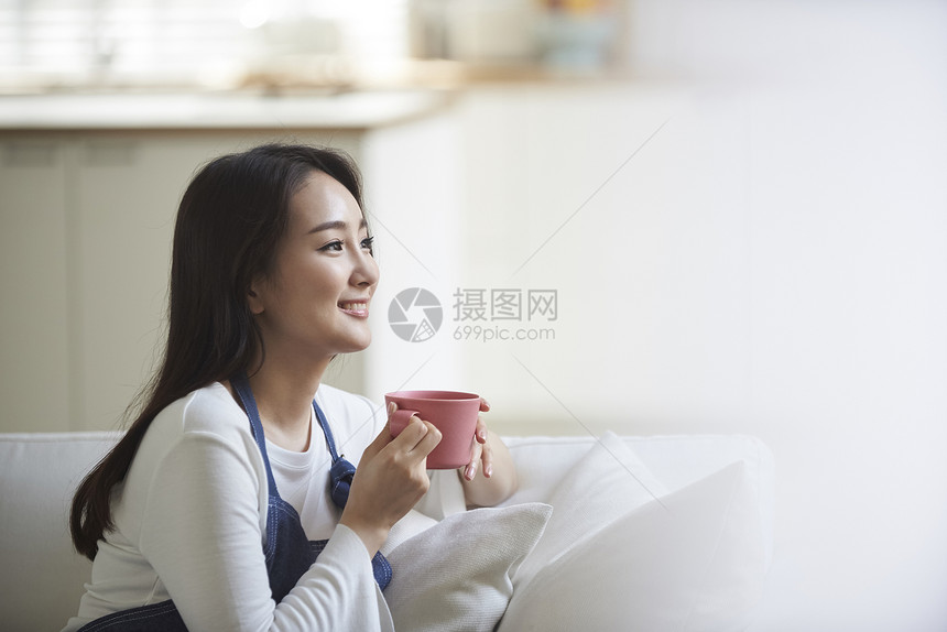 捧着杯子看向窗外的年轻女性图片