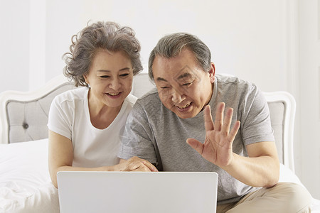 卧室里拿着笔记本电脑视频通话的老年夫妇图片
