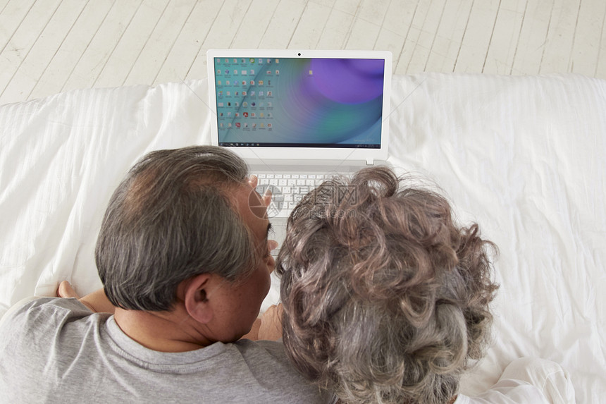 床上看笔记本电脑休息放松的老年夫妻图片