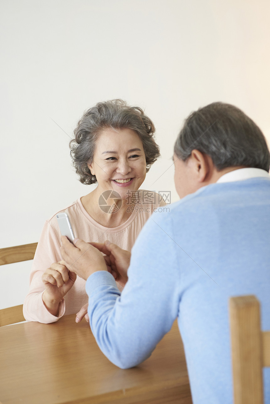 餐桌上看着手机微笑的夫妇图片