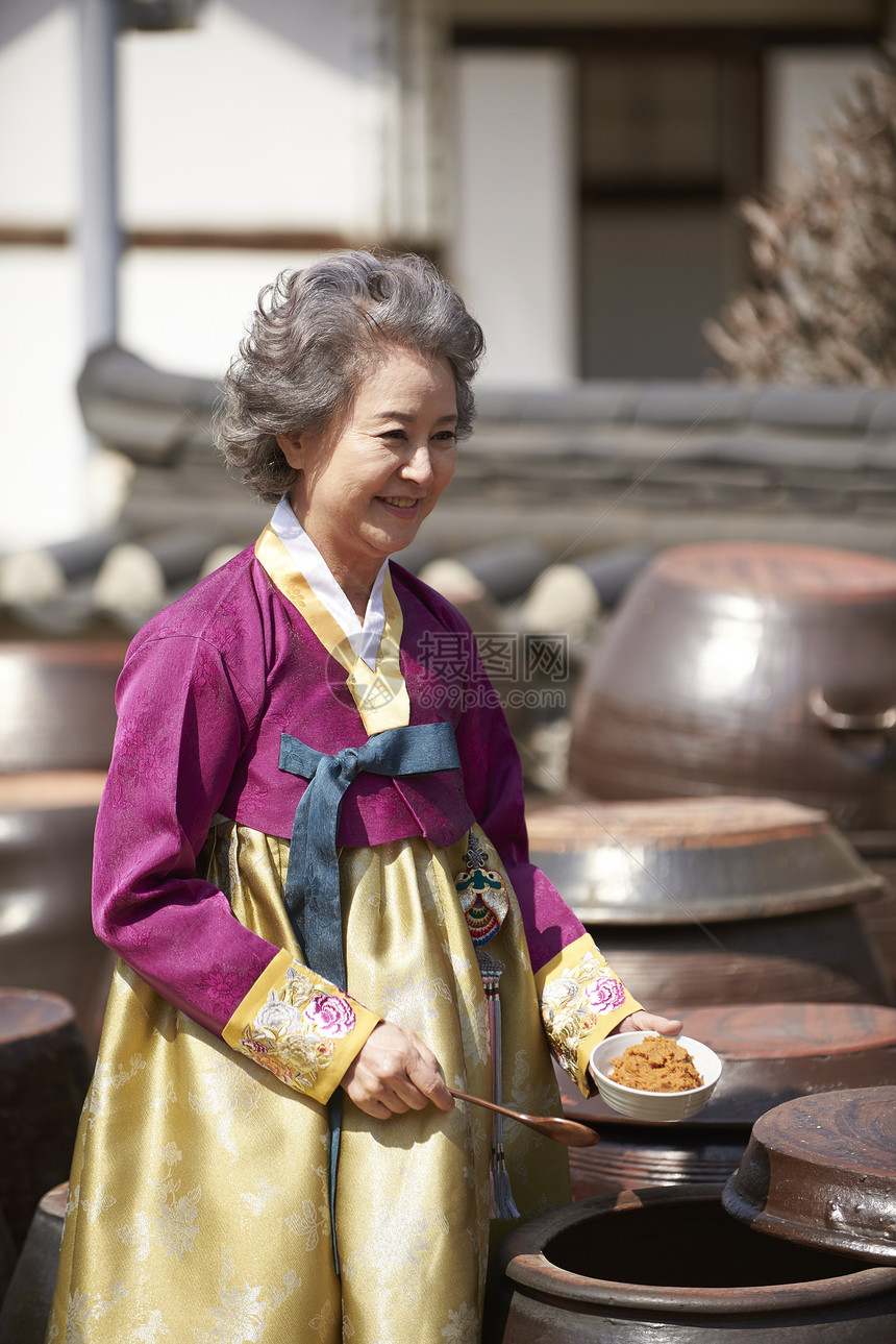穿着传统服装酱缸里舀酱料的老年女性图片
