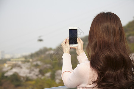 拿着手机拍摄风景的女性背影图片