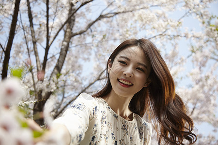 春日站在樱花树下开心的年轻女性图片