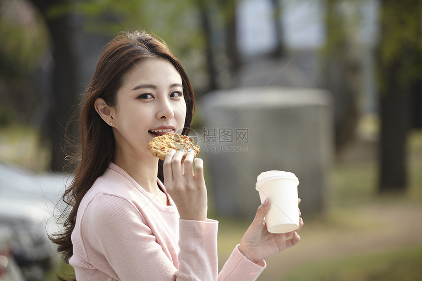 户外拿着咖啡吃着饼干的年轻女子图片