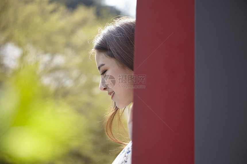 躲在墙后微笑的年轻女子图片