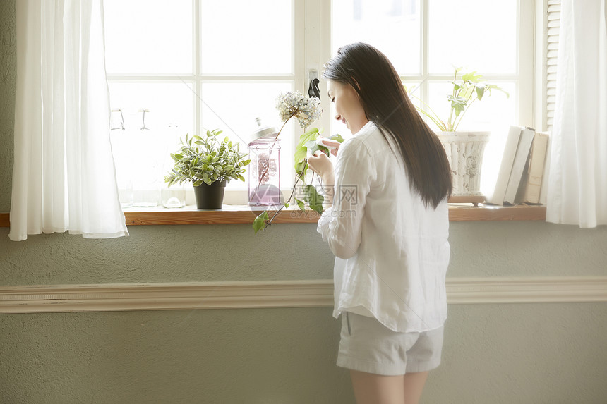 站立在窗口看着植物的居家女性图片