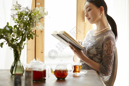 坐在窗边阅读享受下午茶的女性图片