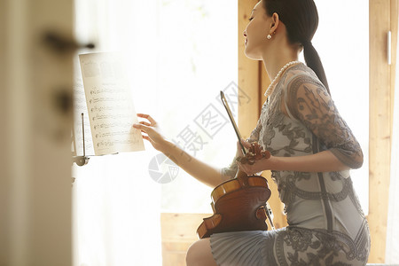 拿着小提琴翻阅着琴谱的优雅女性图片
