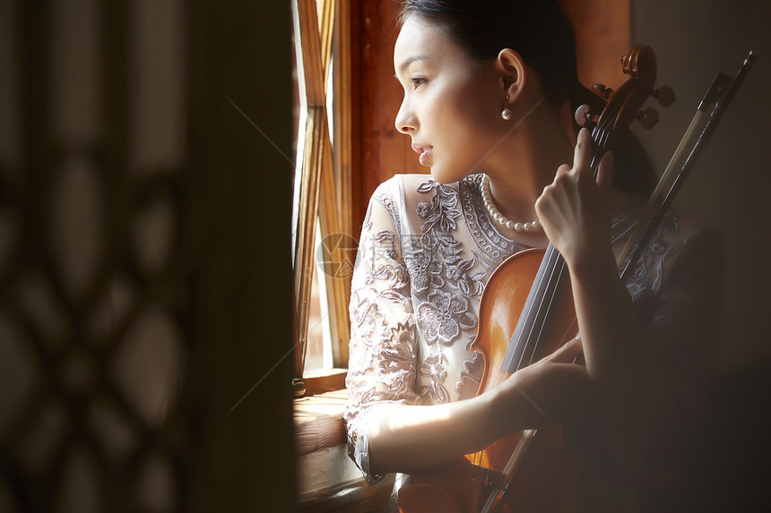 窗边抱着小提琴向外看的女性图片