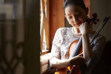 抱着小提琴坐在窗边的成熟女性图片