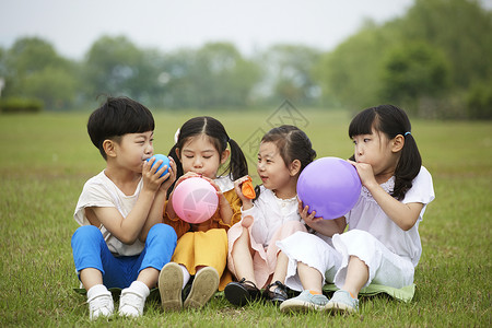 坐在草坪上吹气球的孩子们背景图片