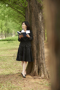 站在树下读书的成年女子图片