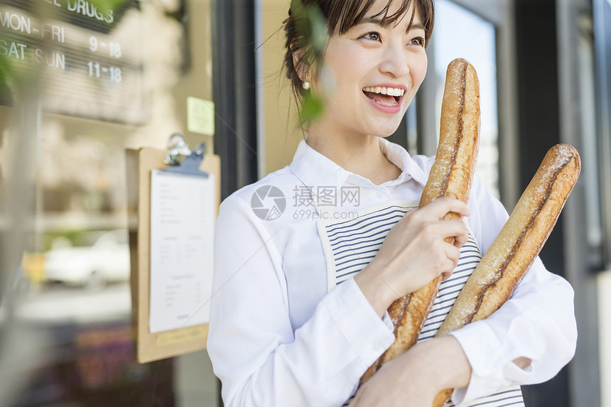 抱着新鲜出炉的法式面包微笑的年轻女性图片