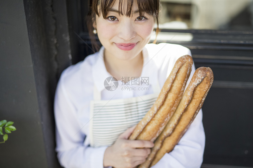 抱着新鲜出炉的法式面包微笑的年轻女性图片