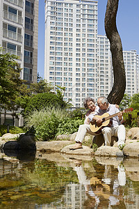 坐在河边岩石上弹吉他的退休老年夫妇图片