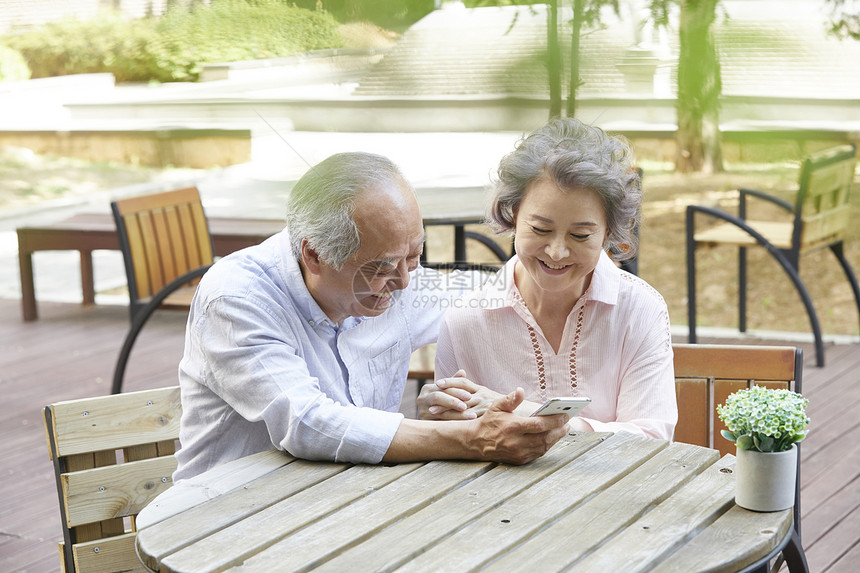 公园里看着手机微笑的老年夫妇图片