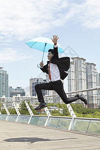 撑着蓝色雨伞跳跃的成年男子图片