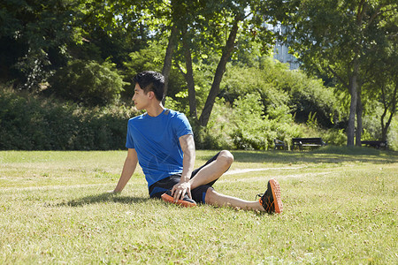 草坪上拉伸运动的男青年背景图片