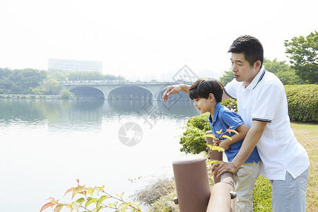 父子二人趴在河岸边上的栏杆上图片