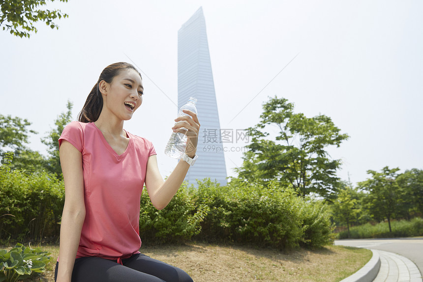 坐在长凳上喝水的青年女性图片