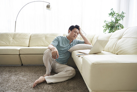 疲倦的男人靠在沙发旁看电脑图片