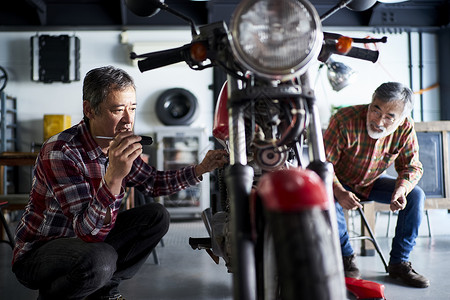 蹲坐修理摩托车的老人图片