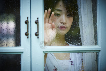 穿过窗口窗格打碎雨天女人在家里度过背景图片