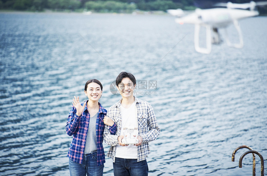 站在湖泊边玩无人机的情侣图片
