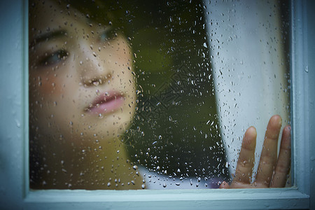 下雨天站在窗户前发呆的孤独女性图片