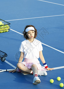 穿着运动服坐在网球场上的年轻女性图片