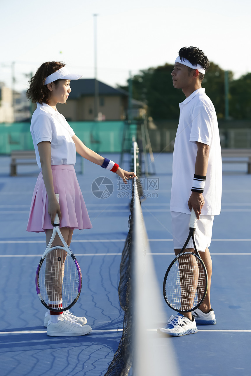 网球场上面对面站着的青年情侣图片
