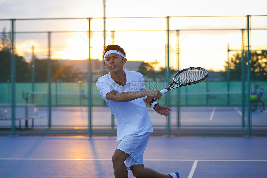 夕阳下户外网球场打网球的成年男子图片