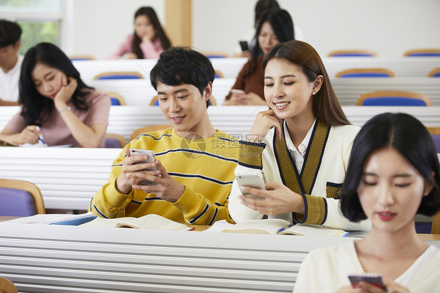 课堂上看着手机微笑的青年男女图片