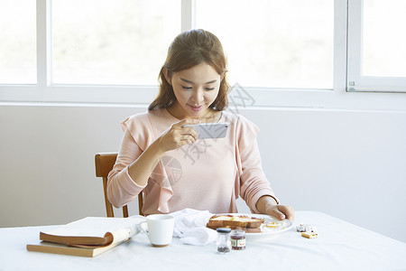 年轻女子拿着手机拍摄食物照片图片