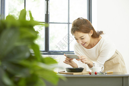 厨房里年轻女子拿着手机拍照图片