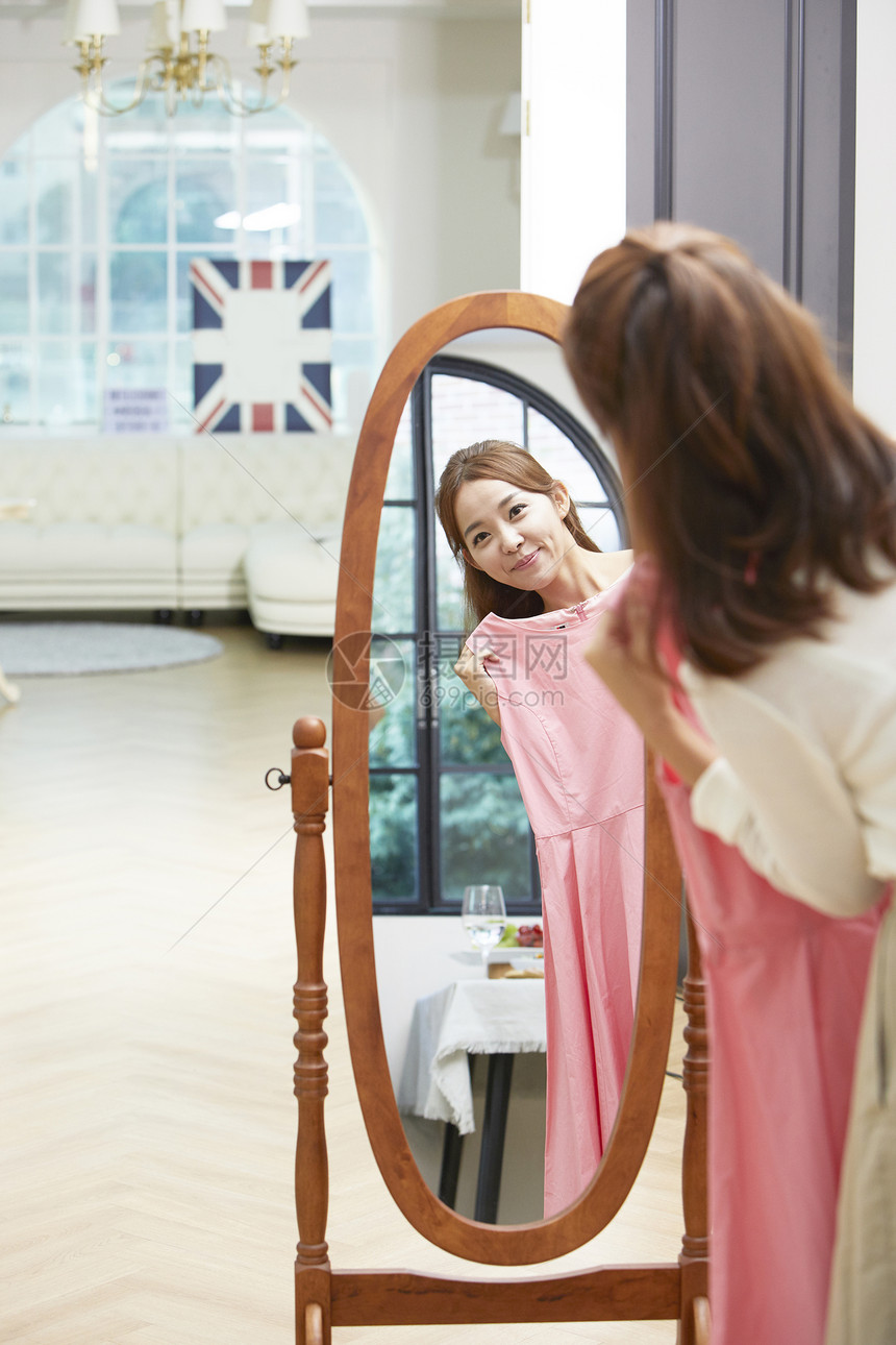 站在镜子前拿着粉裙子的年轻女性图片
