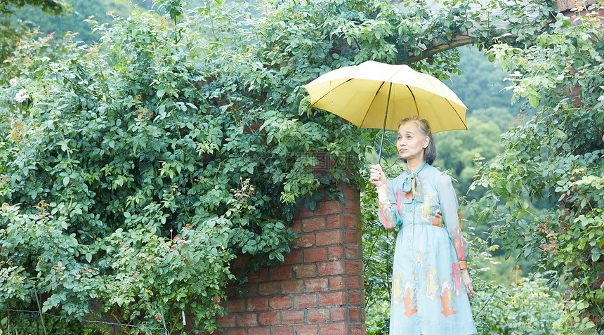 拿着一把伞的老年妇女在庭院里图片
