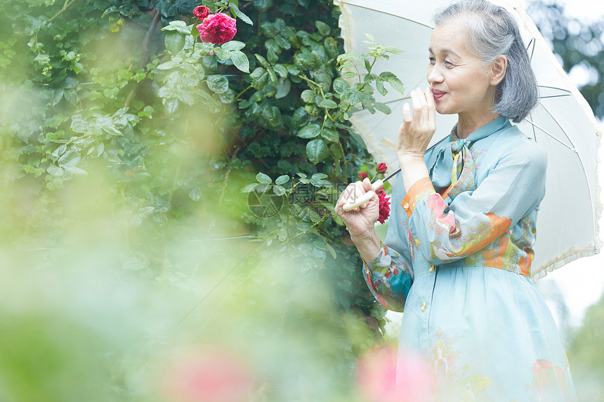 拿着遮阳伞的老年妇女在庭院里摘花图片