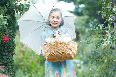 拿着遮阳伞的老年妇女在庭院里摘花背景图片
