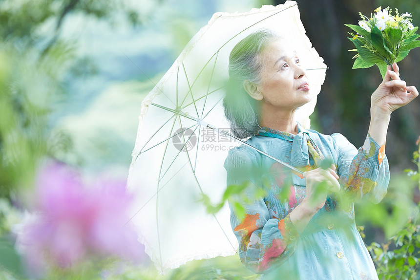 拿着遮阳伞的老年妇女在庭院里赏花图片