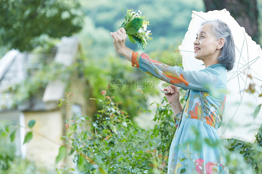 时髦老年的人类拿着遮阳伞的资深妇女在庭院里图片