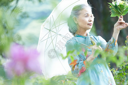 拿着遮阳伞在庭院里散步的老年女性图片