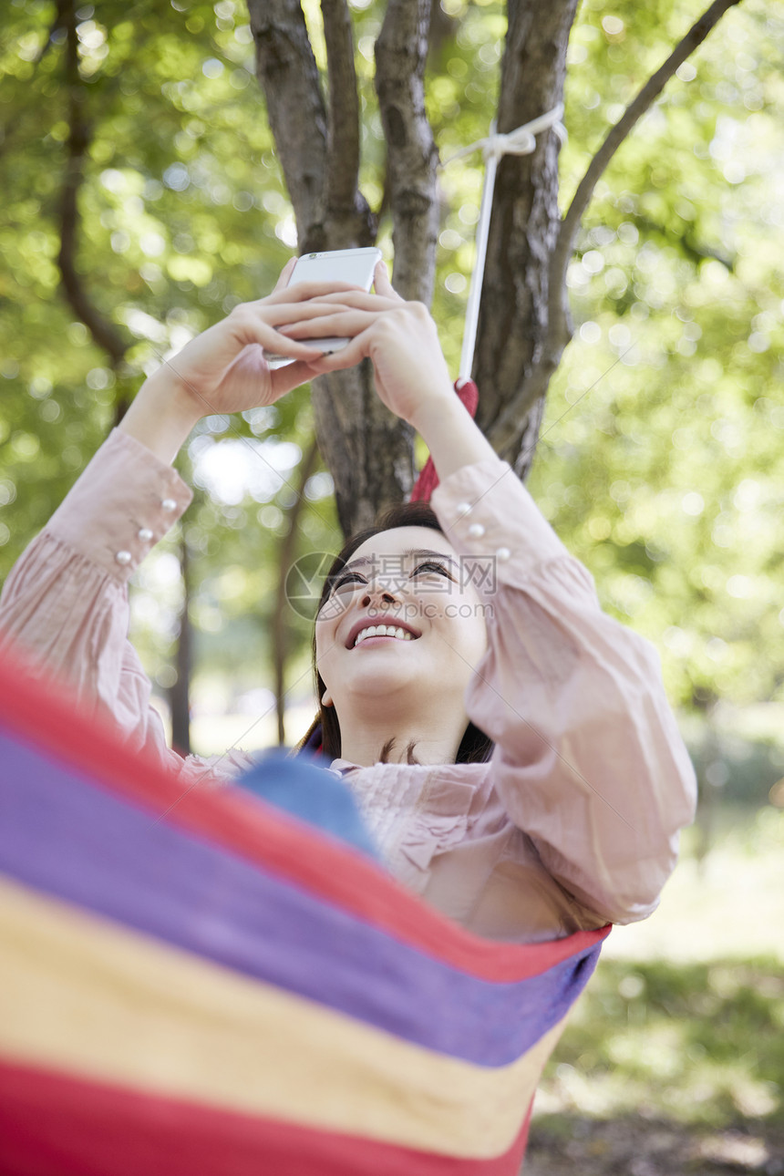 吊床上玩手机开心的年轻女性图片